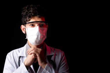 Salgın sırasında siyah arka planda gözlüklü ve maskeli bir doktor. Ev konseptinde kal.