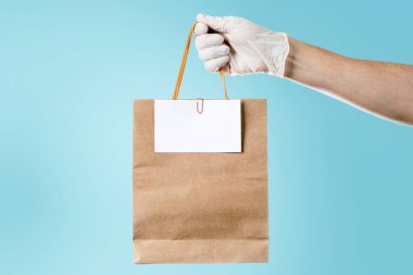 Paket teslimatçısı elinde biletle bekliyor. Teslimatları, bakkaliyeleri ve erzakları hesaba katın. Cyan arkaplanı.