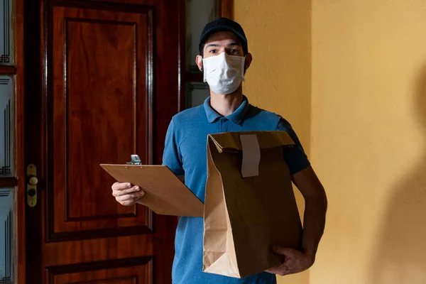 Delivery man with mask holding bag and spreadsheet for delivery verification.