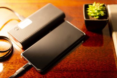 Tahta yatak başlığında harici bataryası olan bir cep telefonu. Teknik Aygıt Paylaşımı.