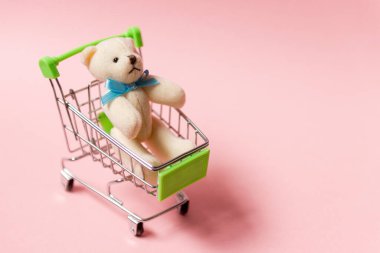 Pembe arka planda oyuncak ayıyla alışveriş arabası. Çocuk günü konsepti.