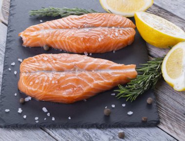 Tahtada limon ve biberiyeli iki taze çiğ somon balığı bifteği.