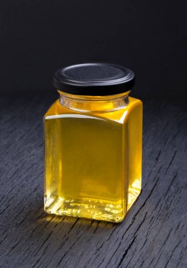 Siyah arka planda şeffaf bir kavanozda bal