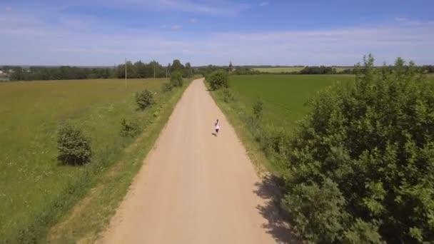 Lány fut az út egy mezőben. Légifelvételek. — Stock videók