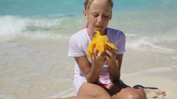 Молодая девушка на пляже ест фрукты манго — стоковое видео