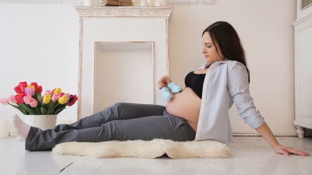 Беременная женщина с детскими туфельками на животе — стоковое видео
