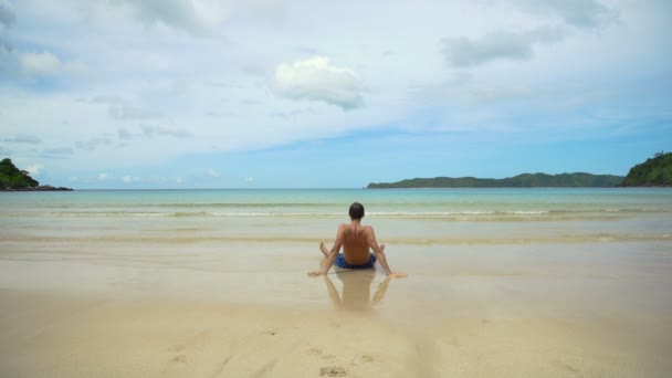 Muž sedí na pláži. — Stock video