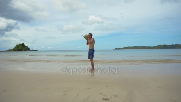 Man drinkt kokosnoot sap uit een moer op een strand van de Oceaan. — Stockvideo