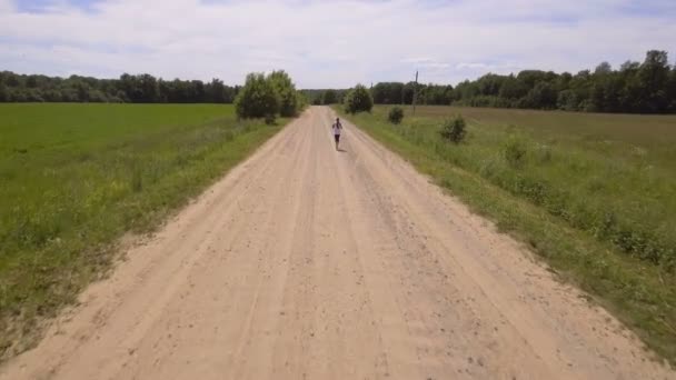 Chica corre en la carretera en un campo. vista aérea . — Vídeos de Stock