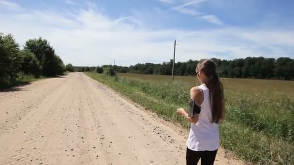 Menina corre na estrada em um campo . — Vídeo de Stock