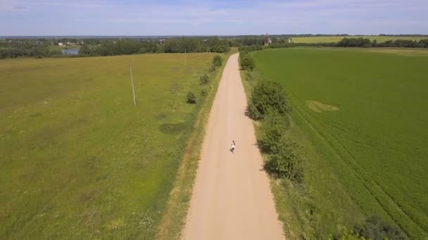 Tjejen kör på vägen i ett fält. Flygfoto. — Stockvideo