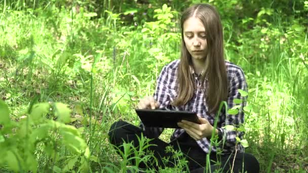 女孩在树林里使用一台平板电脑. — 图库视频影像