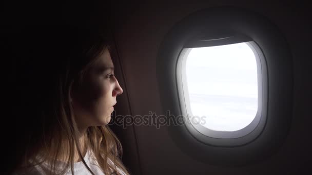 Chica sentada junto a la ventana del avión y mirando afuera. — Vídeos de Stock