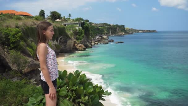 Flickan står på en klippa och tittar på havet. Bali, Indonesien — Stockvideo