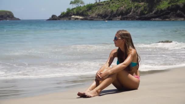 Menina nos óculos de sol senta-se na praia. — Vídeo de Stock