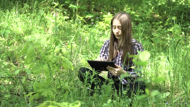 Chica utiliza una tableta en el bosque . — Vídeos de Stock