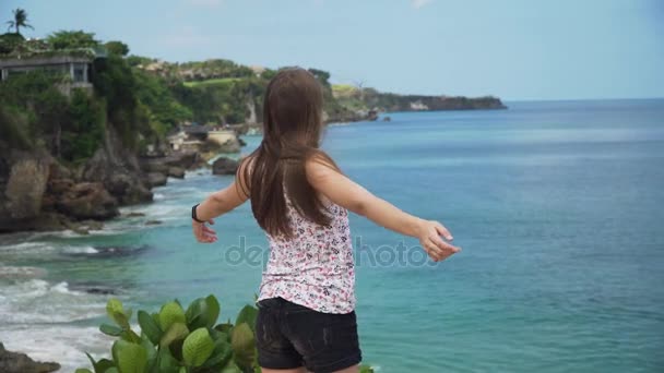 Meisje dat op een klif staat en naar de zee kijkt. Bali, Indonesië — Stockvideo