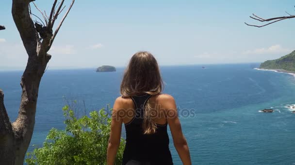 Девушка, стоящая на скале и смотрящая на море. Бали, Индонезия — стоковое видео