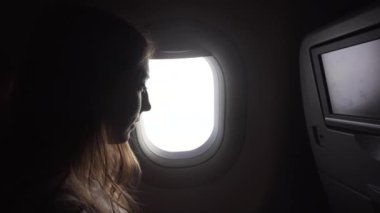 Kız uçak penceresinin yanında oturuyor ve dışarı bakıyor..