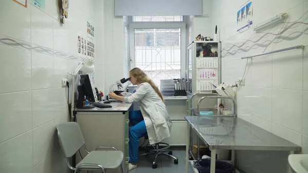 Mulher médico olha em um microscópio. — Fotografia de Stock