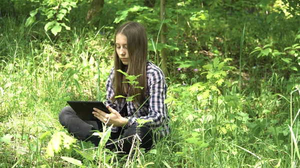 Flicka använder en surfplatta i skogen. — Stockfoto