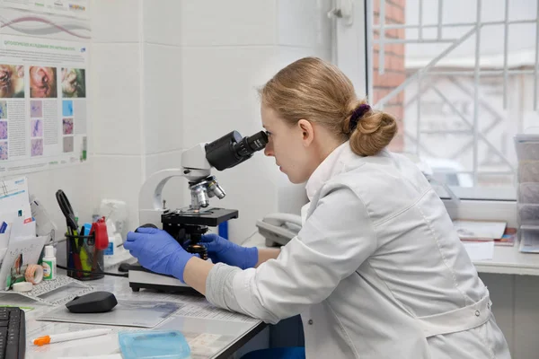 Médico mujer mira en un microscopio. — Foto de Stock