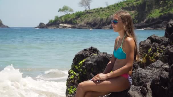A lány leül a sziklára, és a tengert nézi. Bali, Indonézia — Stock videók