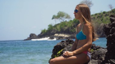 Kız kayaya oturur ve denize bakar. Bali, Endonezya