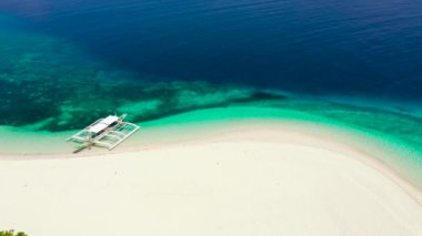 Beyaz kumdan oluşan tropik plaj, üst manzara. Sahilde bir turist teknesi. Sakin plaj sahnesi.