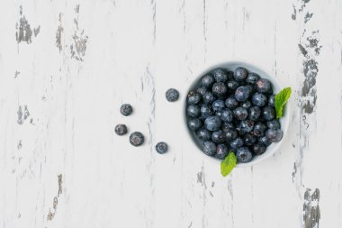 Olgun ve sulu taze yaban mersini kasede nane yaprakları ile süslenmiş beyaz rustik ahşap arka planlar. Üst görünüm