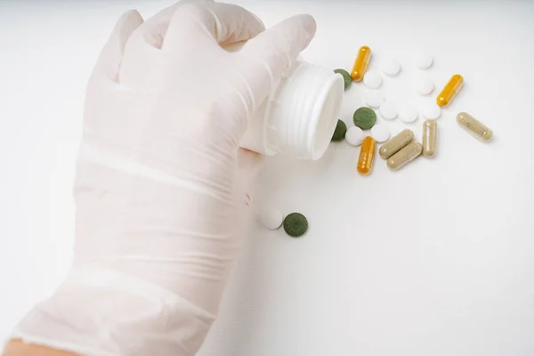 Ręka Medycynie Jednorazowa Rękawica Rozlewając Tabletki Kapsułki Białej Plastikowej Butelki — Zdjęcie stockowe