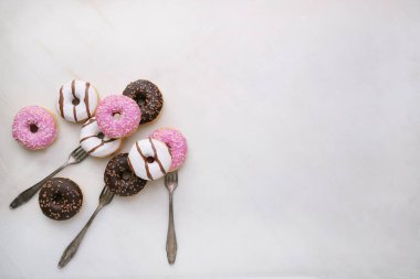 Jöleli, çikolata kaplı ve çatallara serpiştirilmiş donutlar mermer arka planda izole edilmiş. Üst Manzara. Çatal Çılgınlığı seti