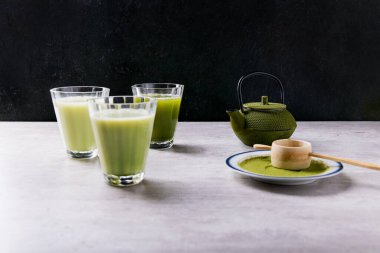 Ev yapımı matcha çayı buğulanmış inek sütü ve hindistan cevizi sütü. Matcha latte için, kibrit tozu ve yeşil metal çaydanlıkla süslenmiş.
