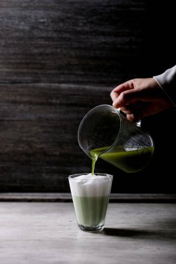 Kibrit çay lattesinin hazırlanması: Bir bardak kibritle kadın elleri buğulanmış süt köpüğüne dökülüyor.