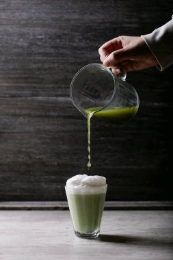 Kibrit çay lattesinin hazırlanması: Bir bardak kibritle kadın elleri buğulanmış süt köpüğüne dökülüyor.