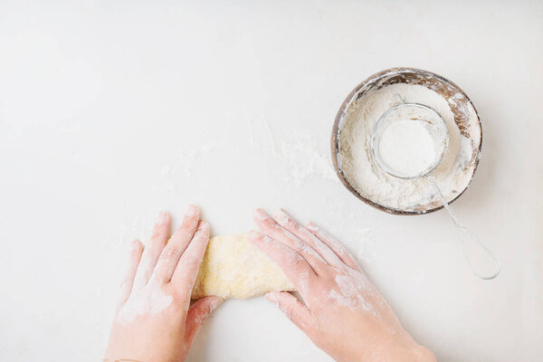 Dough Making Process. Coconut bowl with flour and strainer. Female hand kneading the dough. White background. Top view. 