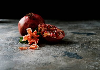 Nar meyveleri, tam ve yarım, kırsal arka planda nar çiçeği dallarıyla süslenmiş. Yan görüş. Kapatın. Seçici odak