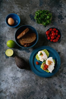 Avokado tostları, haşlanmış yumurta ve eklentiler. Sağlıklı vejetaryen kahvaltısı. Kızarmış ekmek, taze avokado, yumurta, limon, yeşillik ve domates. Üst görünüm