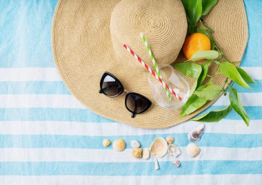 Yaz konsepti. Plaj seti: güneş gözlüğü, deniz kabuğu, pipetli cam ve çizgili plaj havlusunda turuncu şapkalı dal. Üst görünüm.