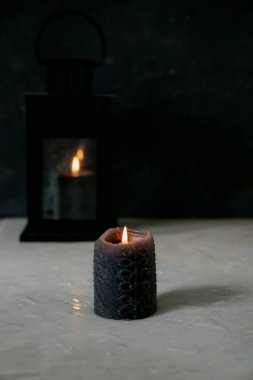 Ön cephede kısmen yanmış siyah mum. Arka planda eski bir fenerde yanan bir siyah mum daha. Seçici odaklanma. Kapat.