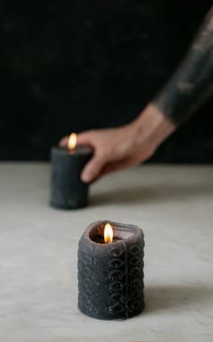 Ön cephede kısmen yanmış siyah mum. Adamın eli arka plana başka bir yanan siyah mum koyuyor. Seçici odaklanma. Kapat.