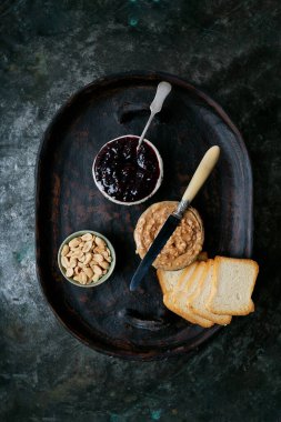 Fıstık ezmesi, ahududu reçeli, kızarmış ekmek dilimleri ve kırsal metal arka planda tepside tuzlanmış fıstık. Üst Manzara. Kahvaltılık sandviçler..