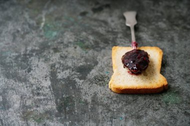 Bir kaşık ahududu reçeli, kızarmış ekmeğin üzerinde, rustik metal zemin üzerinde. Seçici odaklanma. Kahvaltılık sandviçler..