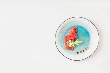 Beyaz zemin üzerinde roka yaprağı ve parmesan peyniri ile süslenmiş mermer etli carpaccio. Üst görünüm. 