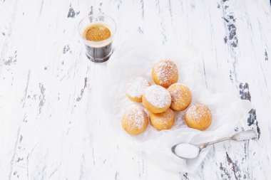 Pişirme kağıdına pudra şekeri serpiştirilmiş taze kızarmış mini çörekler ve rustik ahşap arka plan üzerine espresso. Seçici odak.