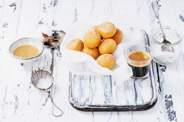 新鲜的油炸小甜甜圈 用粉状糖撒在烤纸上 涂在粗糙的木制背景上 埃斯佩索拍摄 装有浓缩牛奶的陶瓷碗 — 图库照片