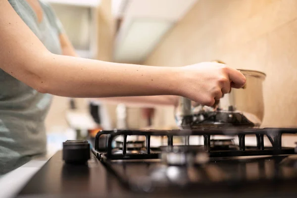 Schöne junge Hausfrau bereitet das Abendessen vor, hält in den Händen einen großen stählernen Topf, der auf dem Gasherd steht. — Stockfoto