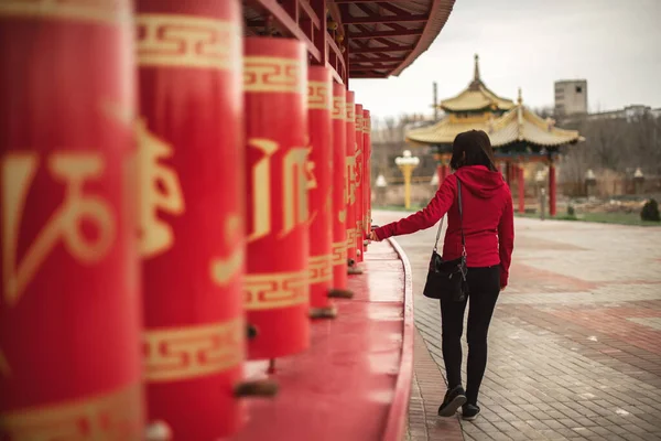 Photo of young beautiful woman turning red prayer wheels in buddhist temple. — Stock Photo, Image