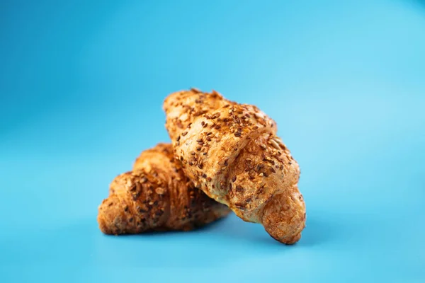 Photo of fresh golden croissants covered sunflower seeds and sesame captured on blue background.