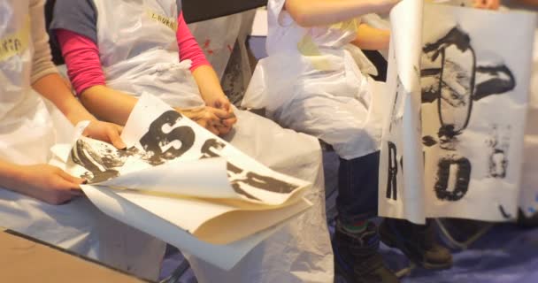 Děti a rodiče sedí a drží obrázky černá písmena razítka na papírových rodinách Malování ve školce animátory bavit děti — Stock video